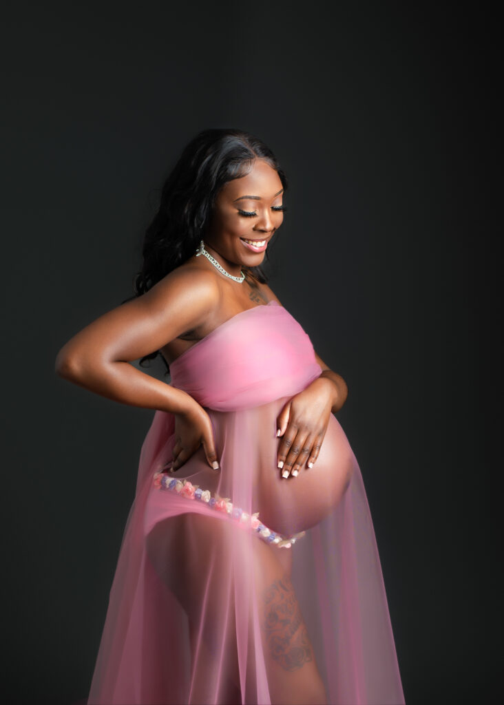 Maternity studio portraits with soft pink fabric wraps, featuring natural, confident poses against a black backdrop