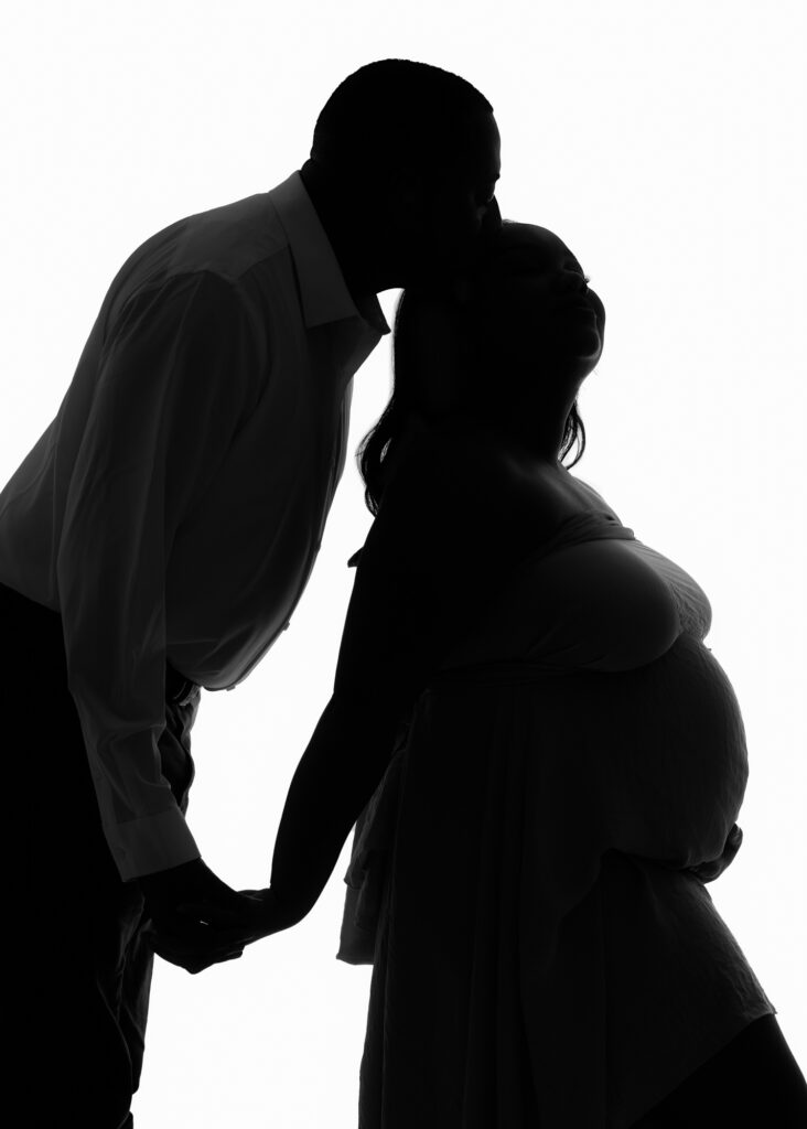 Silhouetted maternity portrait of expectant couple holding hands and leaning in close during a studio photo session