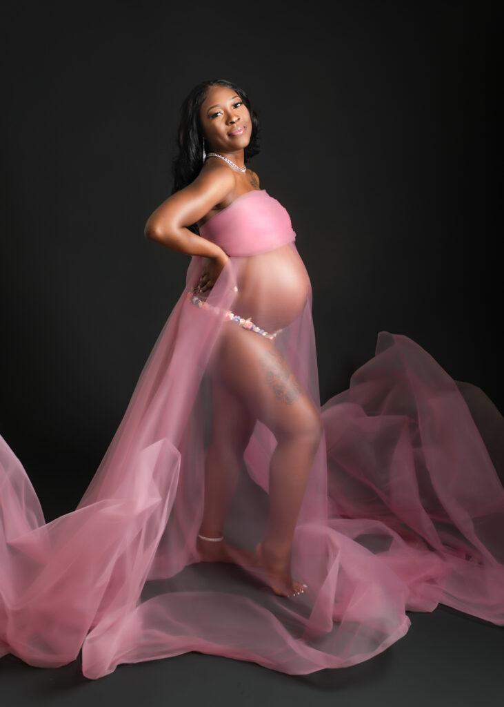 Maternity studio portraits with soft pink fabric wraps, featuring natural, confident poses against a black backdrop