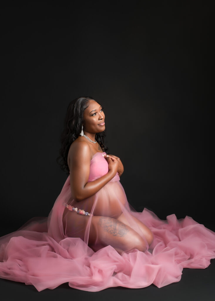 Maternity studio portraits with soft pink fabric wraps, featuring natural, confident poses against a black backdrop
