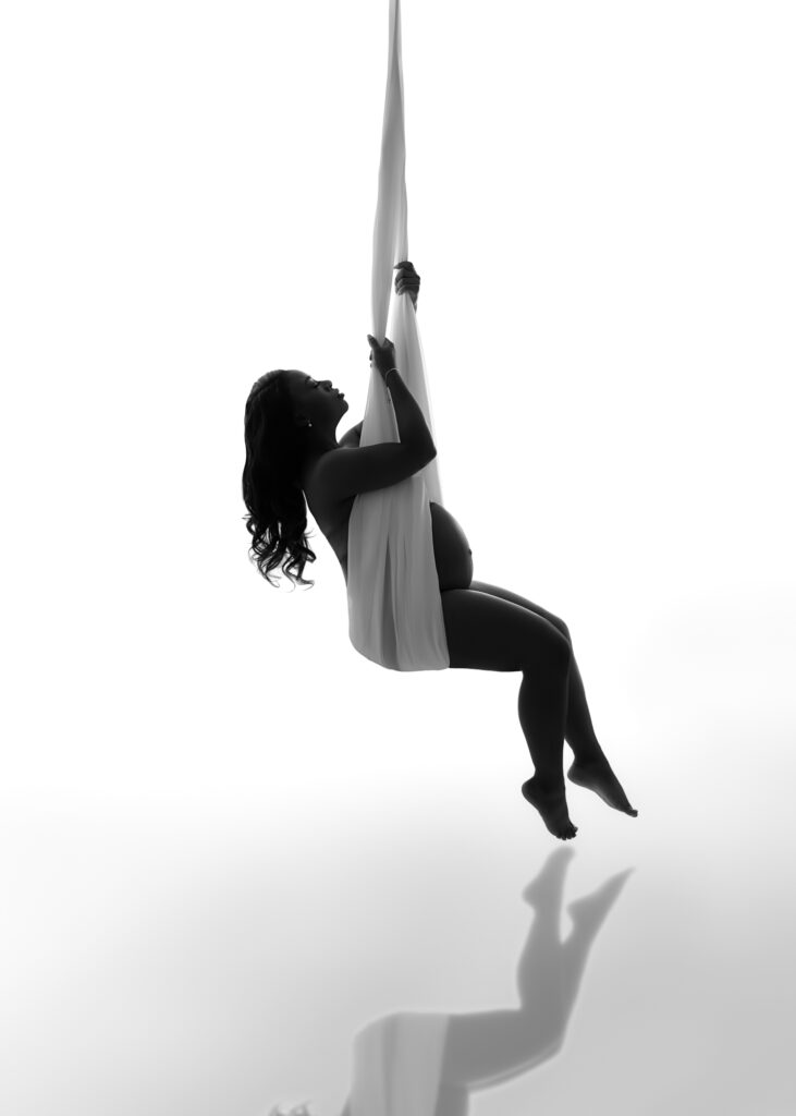 Maternity studio picture of pregnant woman on a fabric swing with the background full of light