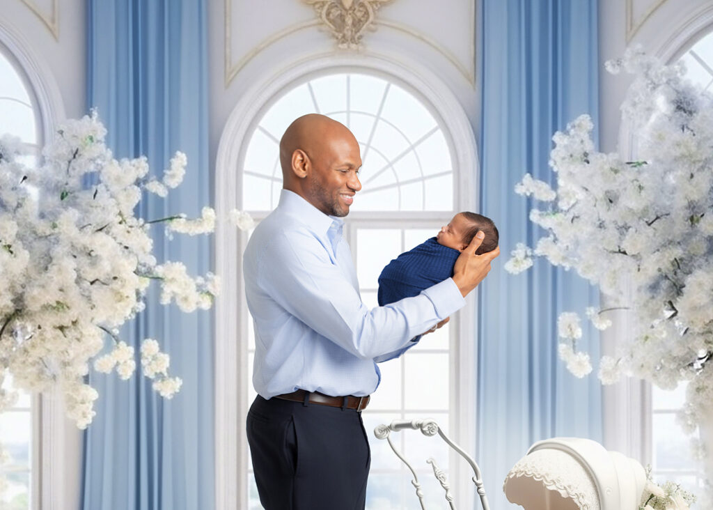 Father lifting his swaddled newborn during a studio session with a newborn photographer in Birmingham — framed by tall floral arrangements and soft blue tones