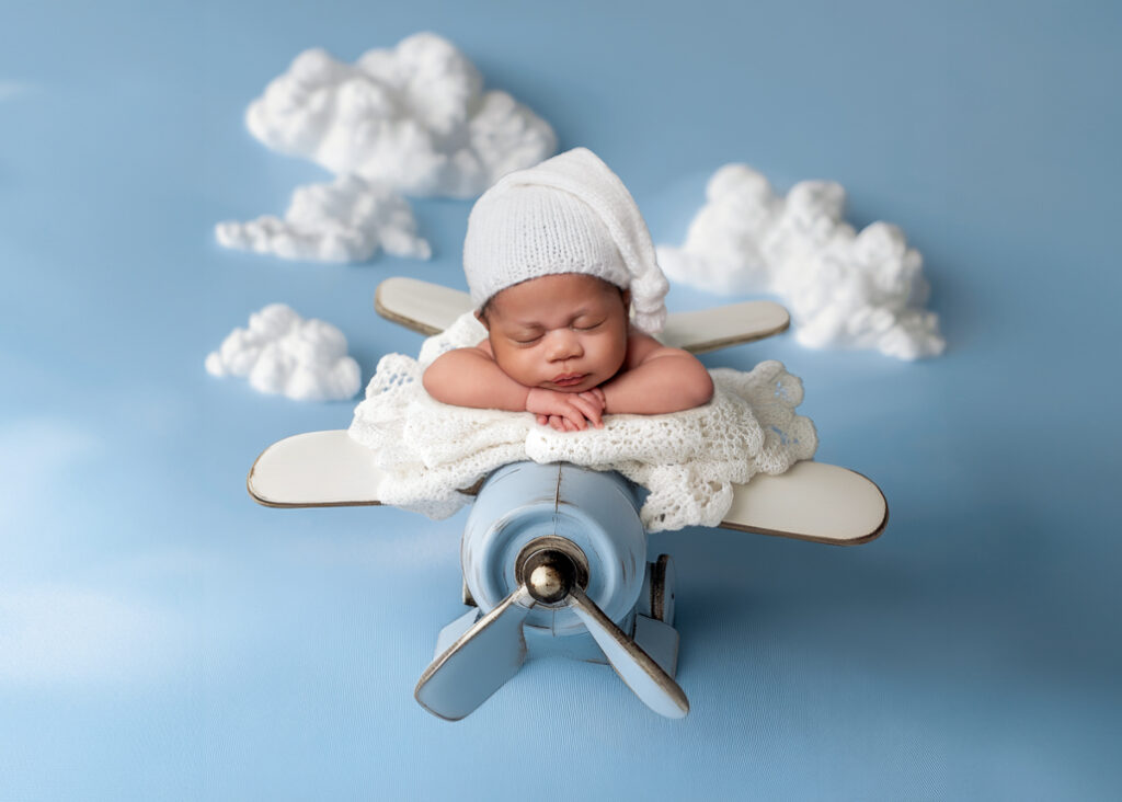 Newborn baby posed in a miniature airplane setup on soft clouds — whimsical portrait by a newborn photographer in Birmingham.
