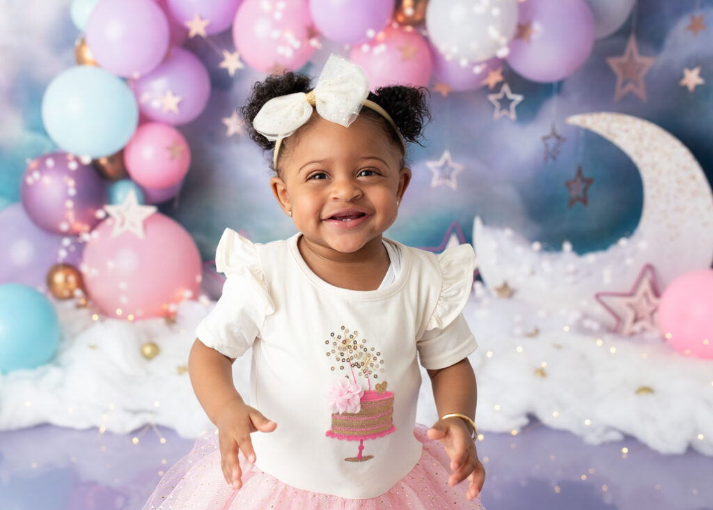 One-year-old girl in pink tutu and moon backdrop for dreamy pastel first birthday photoshoot
