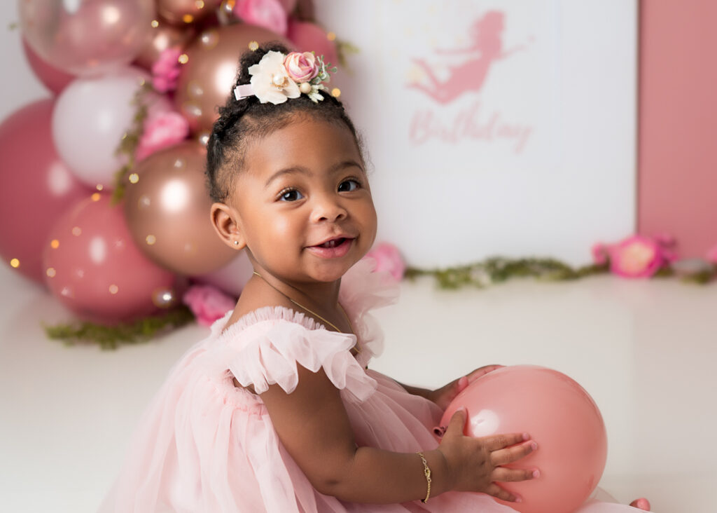 Close-up of baby girl in pink dress smiling during her first birthday photoshoot with fairy-themed decor