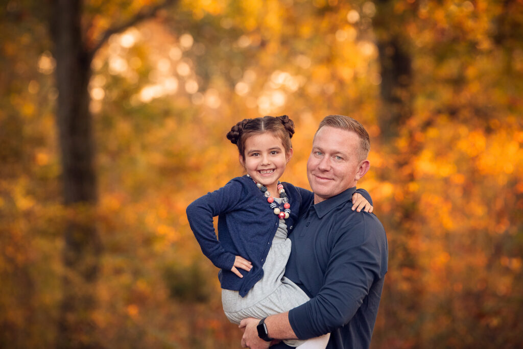 Dad holding his daughter and smiling with soft autumn color behind them in Birmingham, AL.
