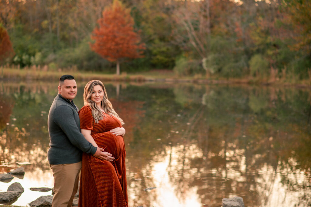 Couple embracing by the lake surrounded by fall colors during maternity mini session in Birmingham.