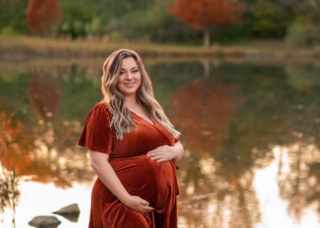 Maternity photo of mom by the lake with autumn reflections during Birmingham fall mini sessions.