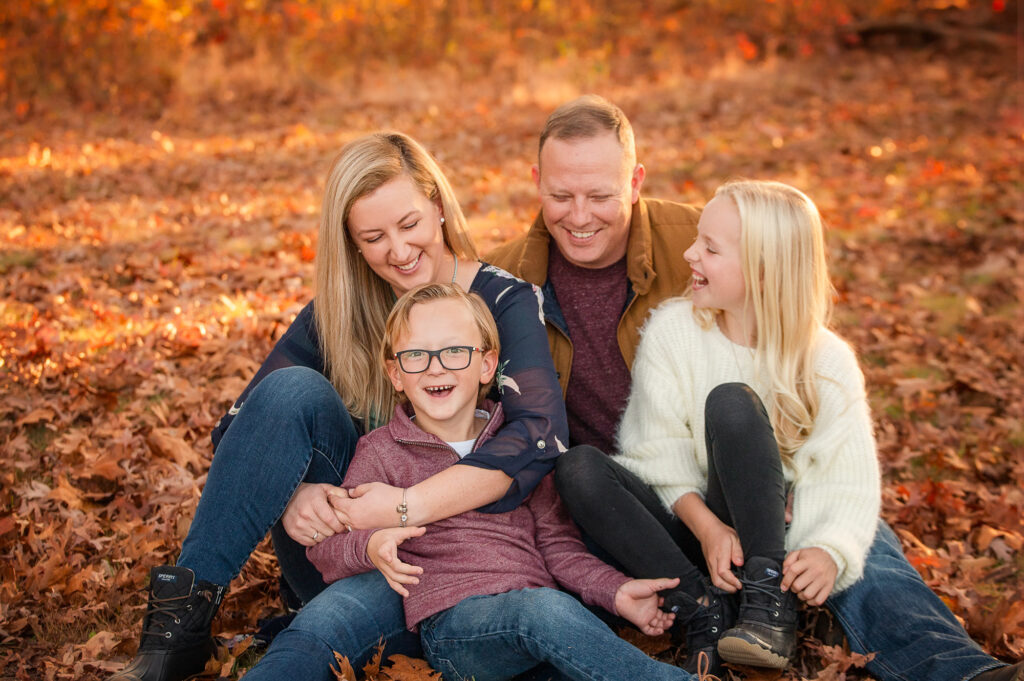 Candid family laughter while sitting in crunchy leaves at a fall mini session in Birmingham, AL.