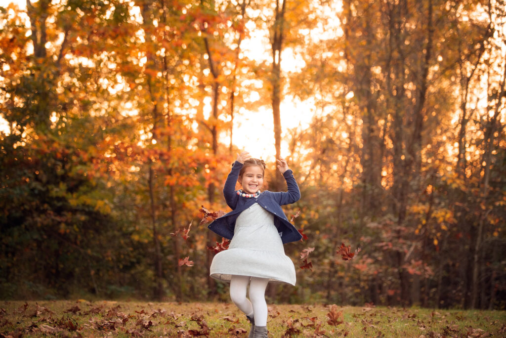 Little girl twirls and tosses leaves at sunset during a fall mini session in Birmingham, AL.