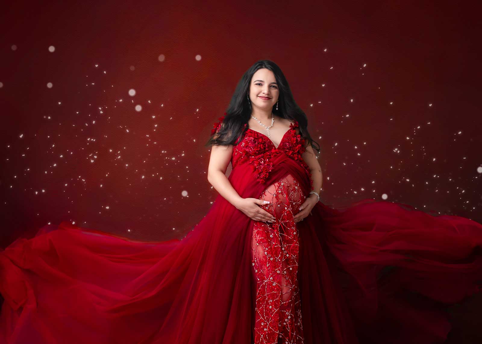 Studio maternity photography in Birmingham featuring a pregnant woman in a flowing red gown on a fine-art backdrop.