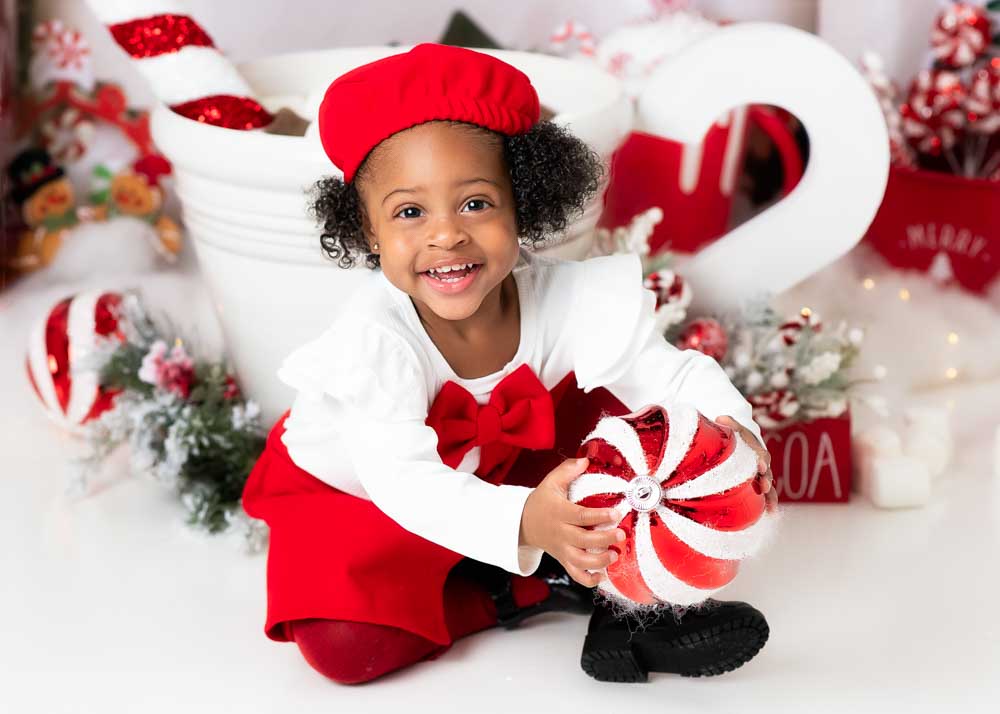 Child close to an oversized white cocoa mug, holding a peppermint ornament on a festive studio set in Birmingham, AL.