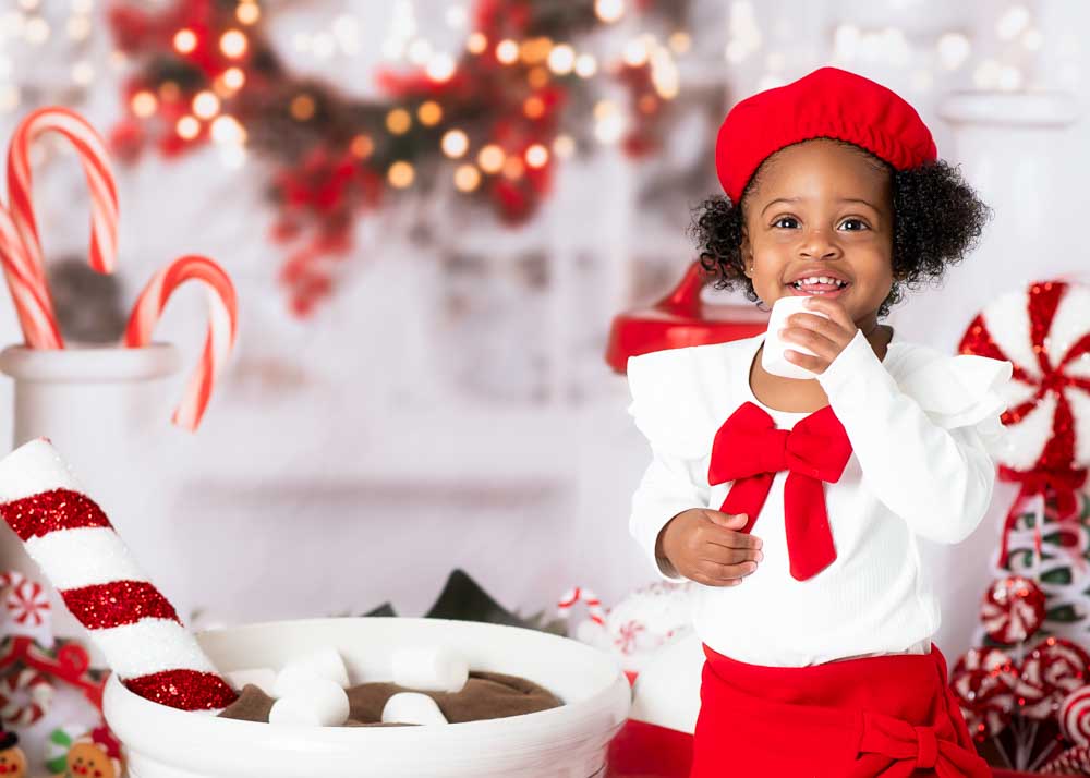 Little girl in a red beret holding a marshmellow beside an oversized mug and candy canes on the Hot Cocoa studio set in Birmingham, AL.