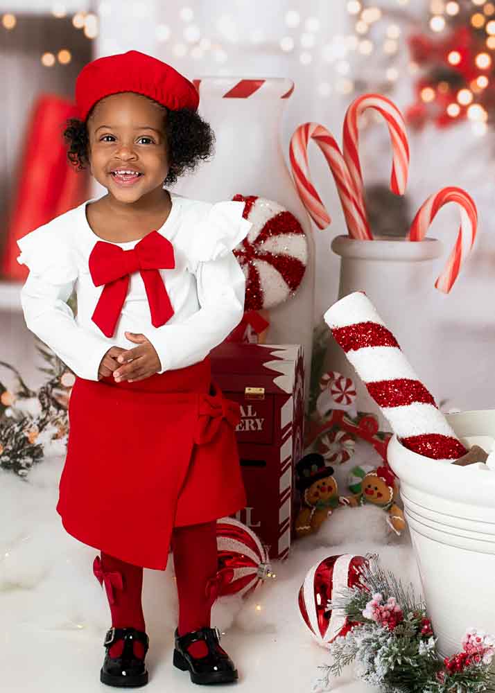 Full-length portrait of a toddler in a red skirt and beret standing on the Hot Cocoa set with peppermint décor, Birmingham, AL.
