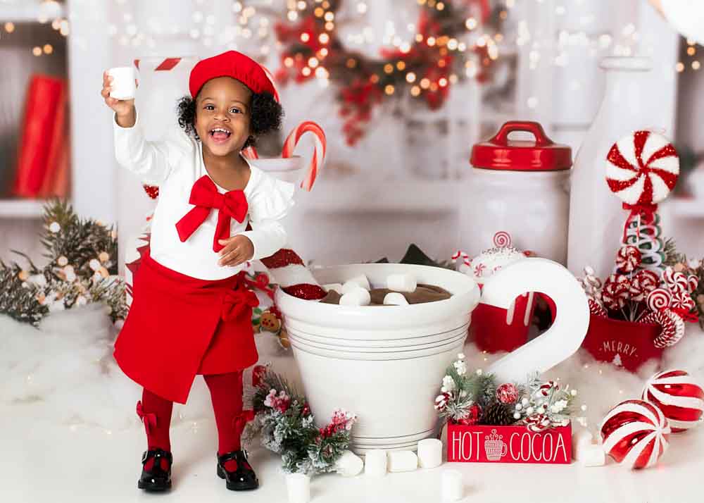 Child holding a jumbo marshmellow beside an oversized hot cocoa mug and marshmallows on a peppermint studio set in Birmingham, AL.