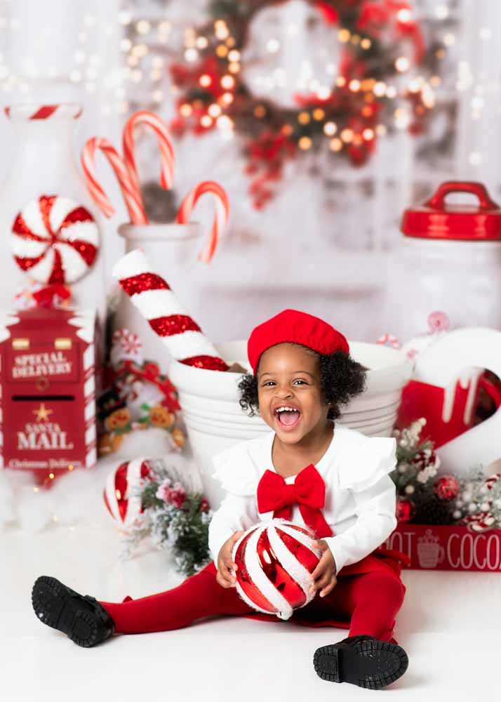 Vertical portrait of a child sitting cross-legged holding a peppermint ornament on the Hot Cocoa studio set in Birmingham, AL.