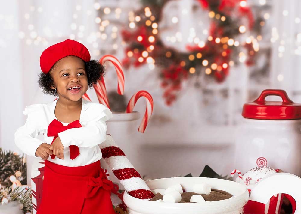 Toddler girl in white blouse and red beret smiling on a festive hot cocoa studio set with candy canes, Birmingham, AL.