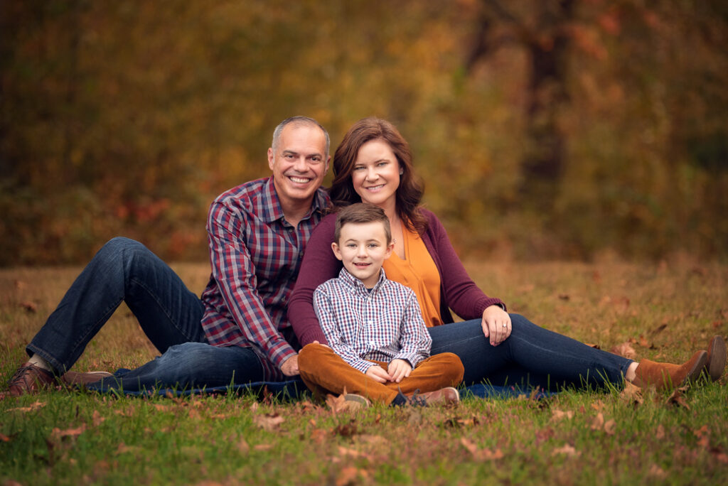 family of three seated dressed in rich burgundy + neutrals