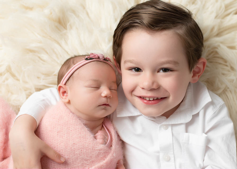 Sibling newborn photos: big brother snuggles newborn sister Emma wrapped in blush in Birmingham studio.