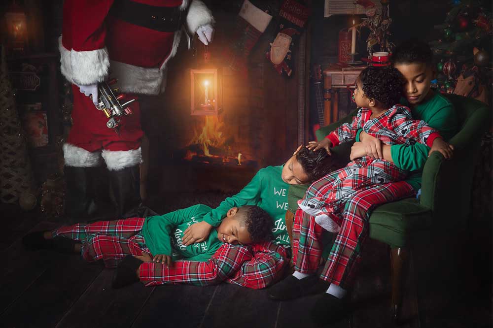 Santa standing beside children resting on a chair and rug in a warm Christmas living room set with candlelight and fireplace ambiance in a Birmingham studio.