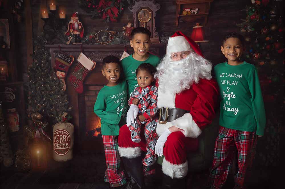 Children gathered around Santa for a classic Christmas portrait in a cozy living room set with a fireplace, stockings, and festive décor in Birmingham, Alabama.