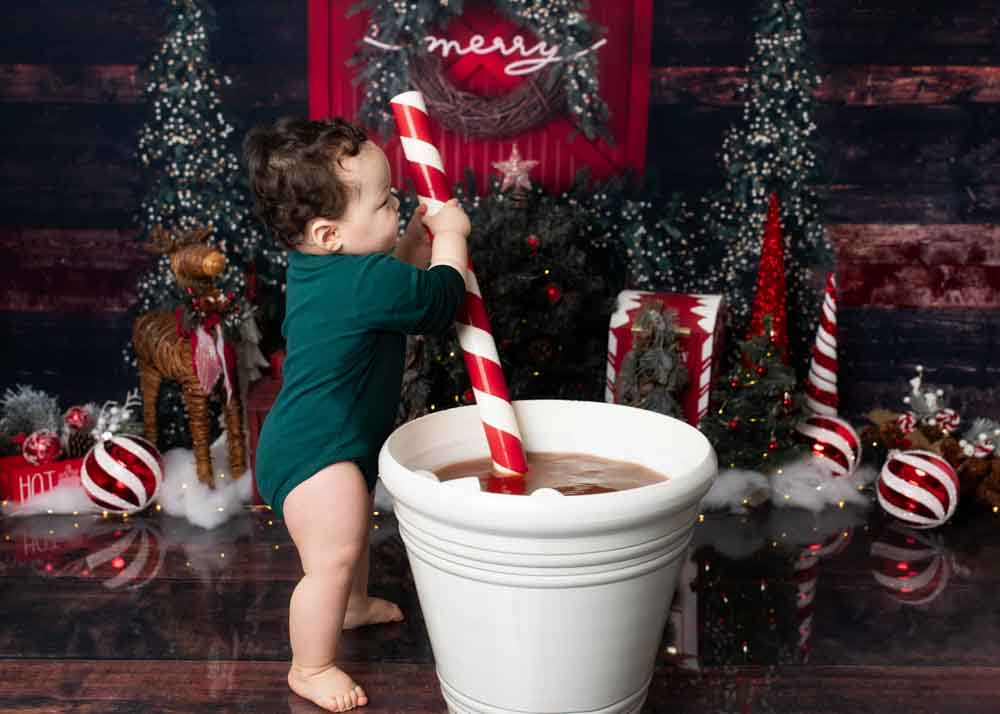 One‑year‑old standing beside a large white cocoa cup prop holding a giant candy cane.