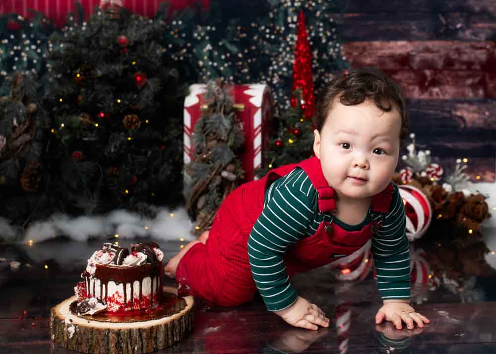 Child crawling toward the camera in a festive Christmas studio with rustic wood backdrop.
