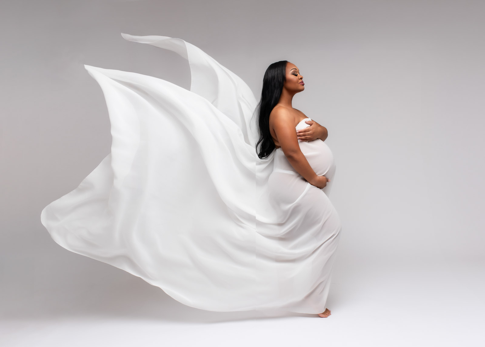 Pregnant mom showing her baby bump in a flowing white gown during her Birmingham maternity photography session.